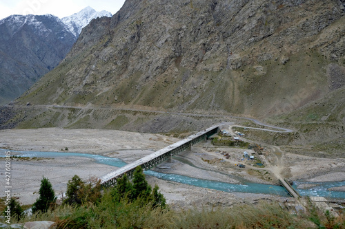 A bridge over a turquoise river in the vast snow-capped mountains of the Himalayas