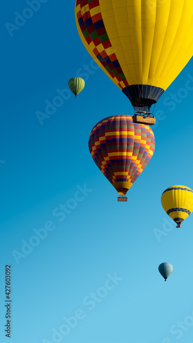 Hot Air Balloons ride for promotion of your travel agency or tour to Cappadocia, vertical landscape. Ballooning trip at clear blue sky background with copy space for text, bottom up view.