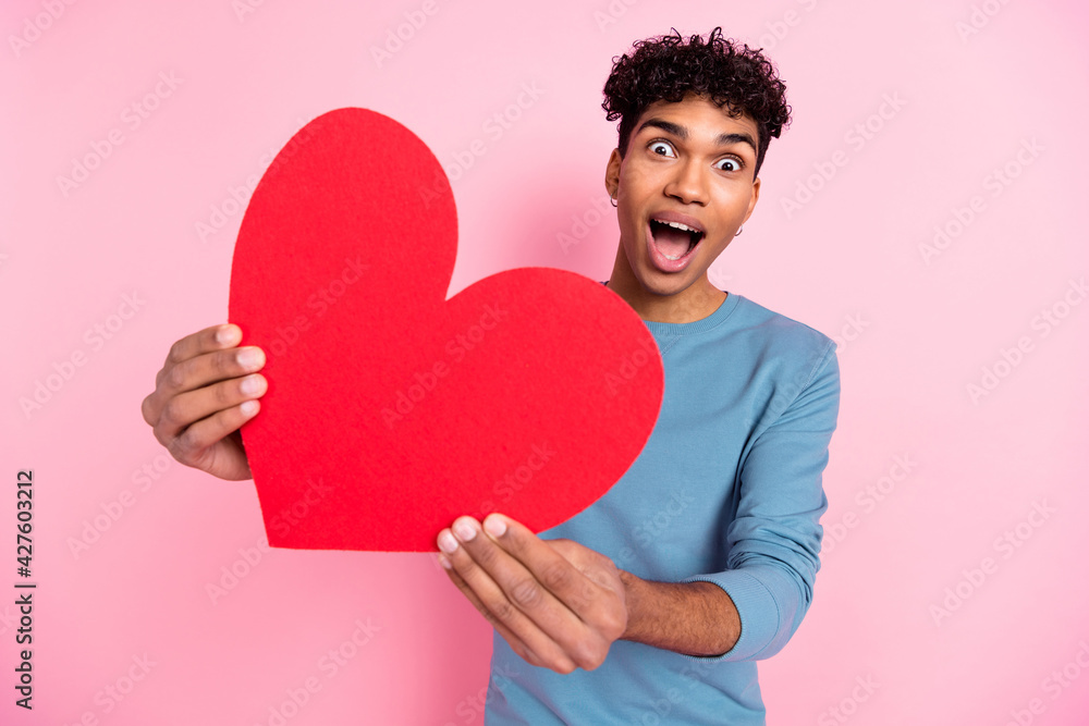 Photo portrait of young amazed guy showing heart shaped postcard on valentines day isolated on pastel pink color background Photo portrait of young amazed guy showing heart shaped postcard on valentines day isolated on pastel pink color background