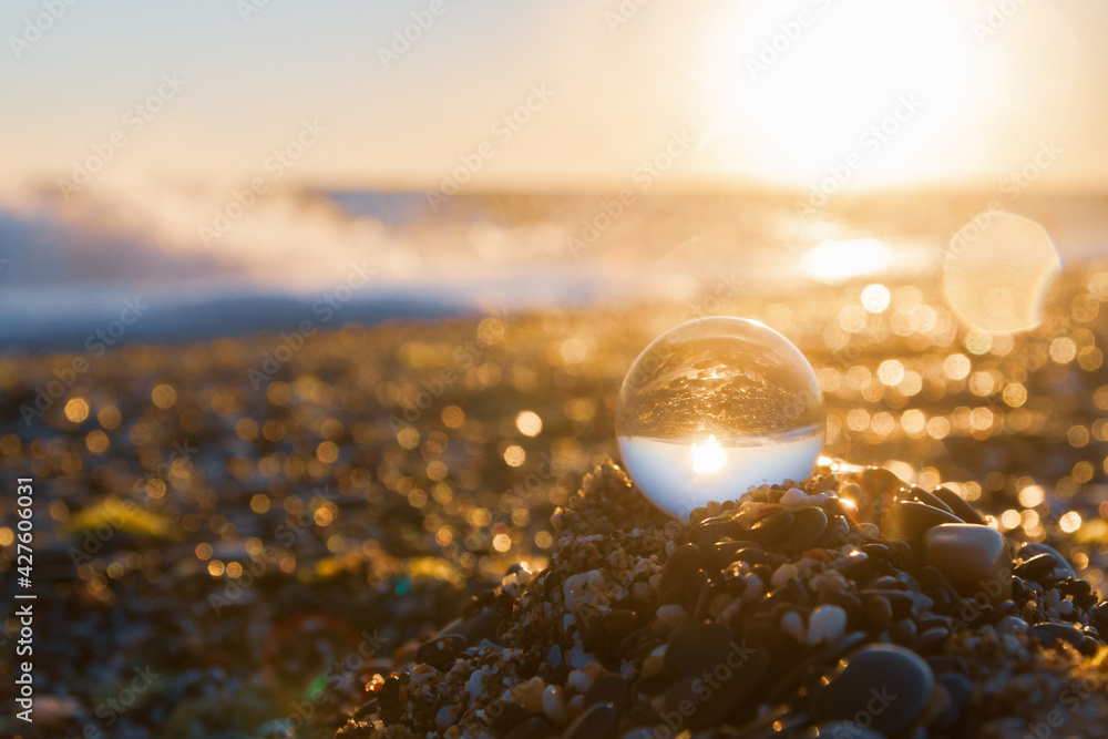 Glass round ball on the beach reflects the sea in summer at sunset Glass round ball on the beach reflects the sea in summer at sunset