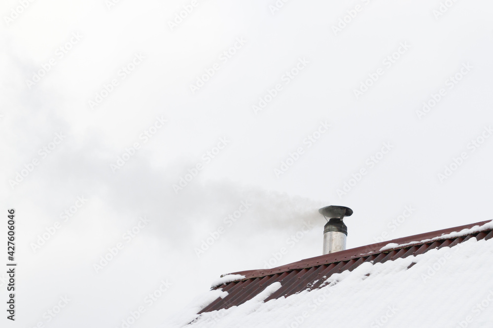 The chimney smokes on the roof of the house