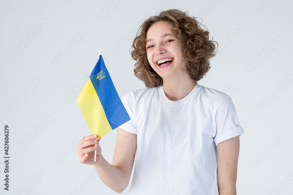 Happy smiling young woman with Ukraine flag on a light background. Studio shot. Happy smiling young woman with Ukraine flag on a light background. Studio shot.
