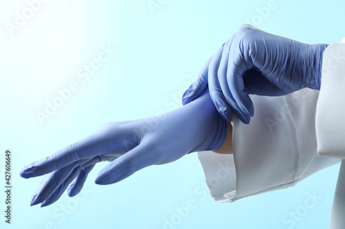 Doctor putting medical gloves on blue background