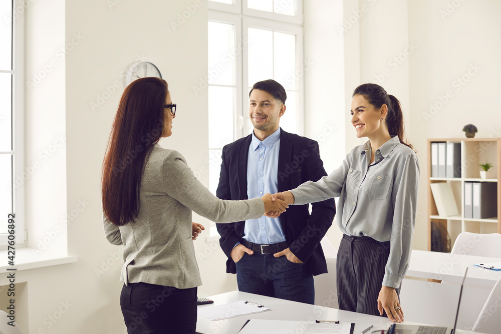 Happy married couple enters into an agreement with a bank employee by taking a loan or mortgage from a bank. Female banking agent shakes hands with customers congratulating new homeowners. Happy married couple enters into an agreement with a bank employee by taking a loan or mortgage from a bank. Female banking agent shakes hands with customers congratulating new homeowners.