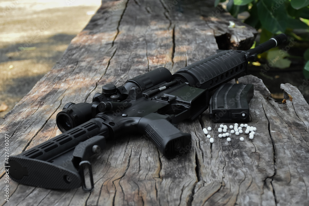 Obraz premium Close up view of black long barreled automatic rifle or bb gun on wooden floors with white plastic bullets. Soft and selective focus.