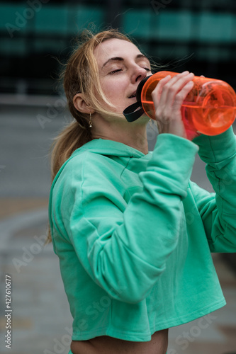 Atractive mature woman wearing activewear is resting after doing exercise and drinking water from a bottle.