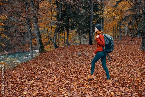 a full-length traveler with a backpack walks in the park with fallen leaves near the river © SHOTPRIME STUDIO