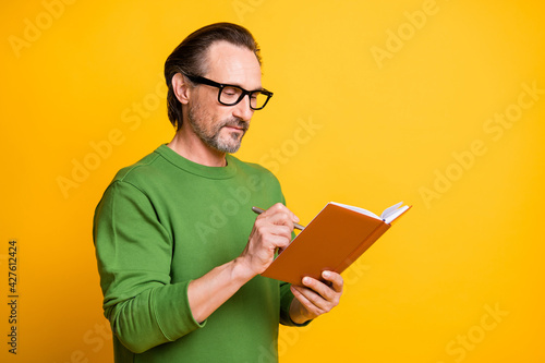 Photo of minded guy hold book pen write wear spectacles green pullover isolated yellow color background
