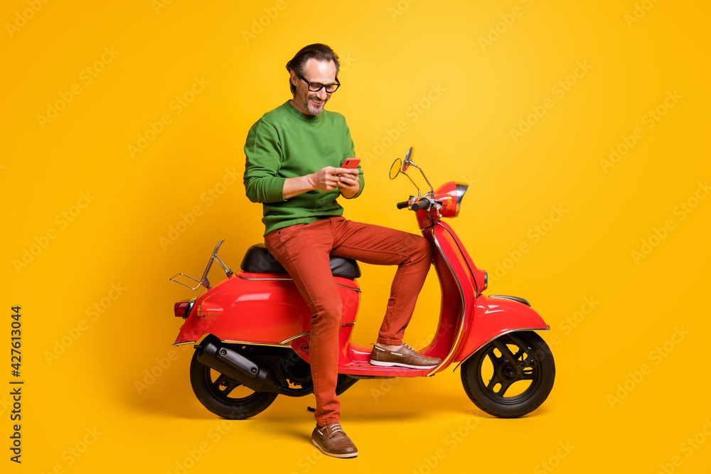 Photo of man hold phone ride scooter wear spectacles green sweater trousers shoes isolated yellow color background Photo of man hold phone ride scooter wear spectacles green sweater trousers shoes isolated yellow color background