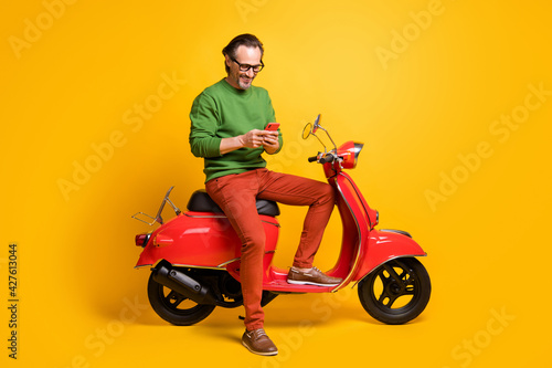 Photo of man hold phone ride scooter wear spectacles green sweater trousers shoes isolated yellow color background