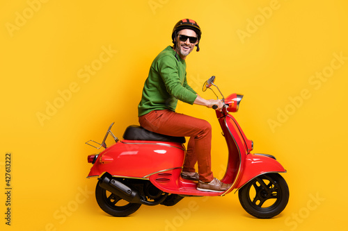 Photo of man drive bike wear helmet sunglass green pullover pants footwear isolated yellow color background © deagreez