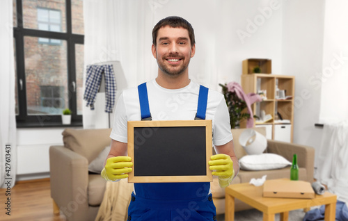profession, cleaning service and people concept - happy smiling male worker or cleaner showing chalkboard over home room background