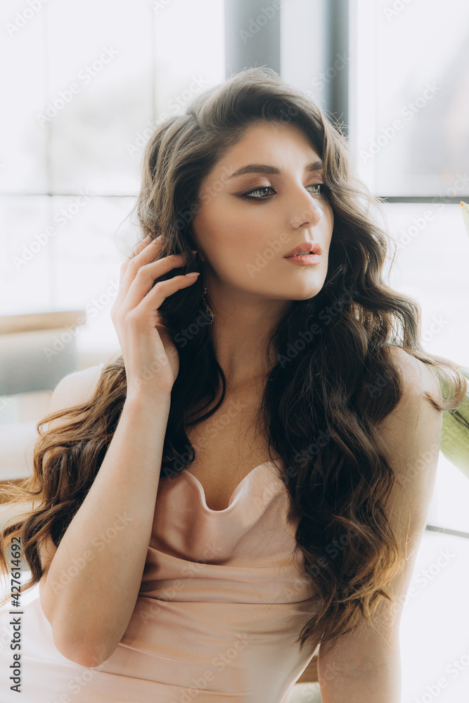 Beautiful, stylish, and elegant girl brunette, model, with makeup and curly hair in a peach-colored silk dress for a magazine photoshoot in fashion style. Beautiful, stylish, and elegant girl brunette, model, with makeup and curly hair in a peach-colored silk dress for a magazine photoshoot in fashion style.
