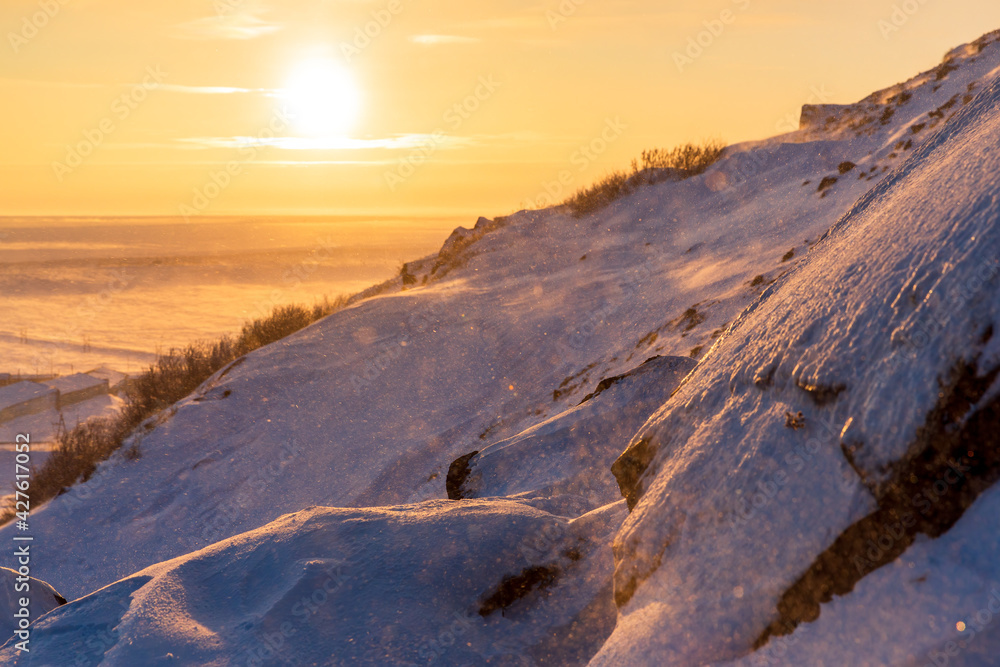 Winter arctic landscape. View from the snow-covered rocky slope of the mountain at a beautiful sunrise over the tundra. Cold windy and frosty weather. Chukotka, Siberia, Russia. Shallow depth of field
