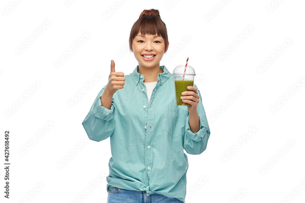 diet, healthy eating and detox concept - happy smiling young asian woman drinking green vegetable juice or smoothie from plastic cup with paper straw showing thumbs up over white background diet, healthy eating and detox concept - happy smiling young asian woman drinking green vegetable juice or smoothie from plastic cup with paper straw showing thumbs up over white background