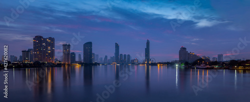 Panorama view of Ferris Wheel and business district in Bangkok city with water reflection at twilight time.