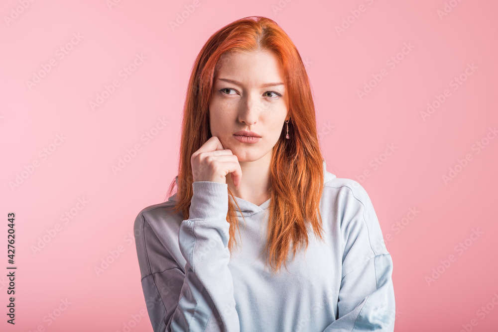 Portrait of a redhead pensive girl in the studio on a pink background Portrait of a redhead pensive girl in the studio on a pink background