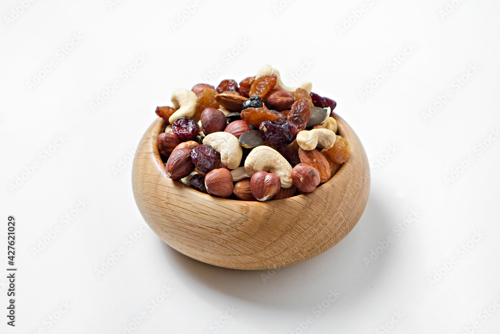 Fototapeta premium Different types of nuts in a wooden bowl isolated on white background. Nutrient dense vegan snacks. Clean eating concept. Close up, copy space for text, top view, flat lay.