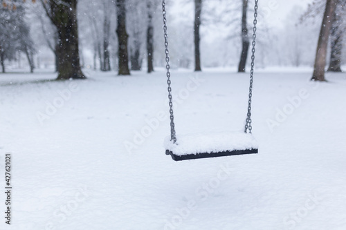 One lonely swing on steel chains, covered with heavy snow, with forest trees in background