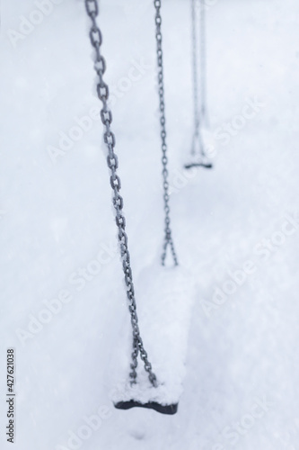 Playground swing set with steel chains covered in heavy snow, abandoned and empty