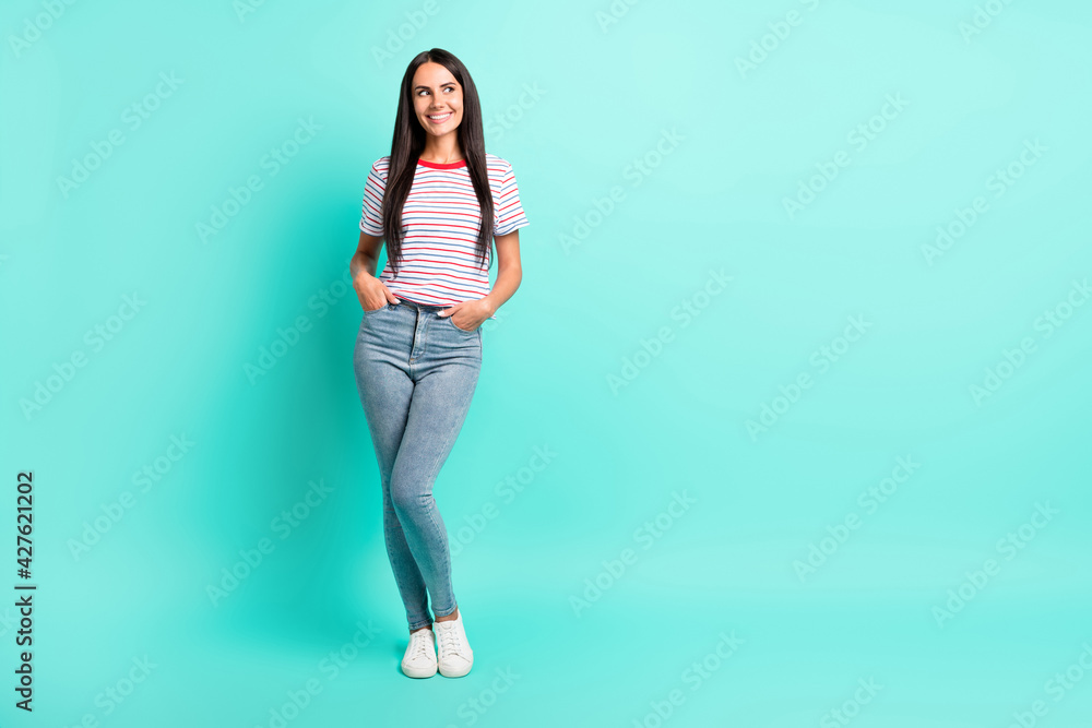 Full size photo of nice brunette optimistic long hairdo lady stand look empty space wear t-shirt jeans sneakers isolated on teal color background Full size photo of nice brunette optimistic long hairdo lady stand look empty space wear t-shirt jeans sneakers isolated on teal color background
