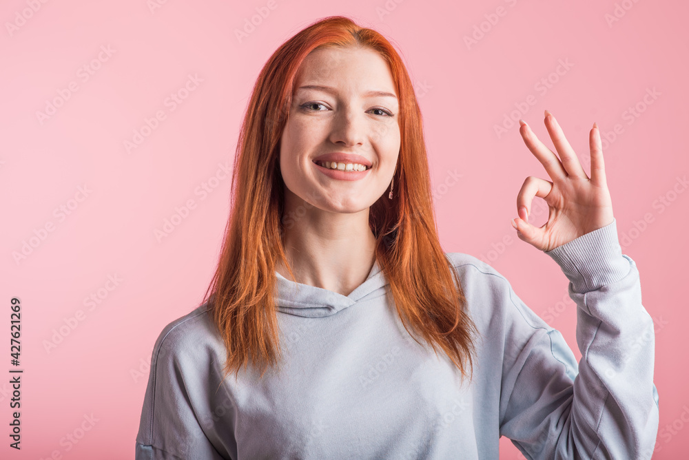 Redhead girl showing Okay gesture in studio on pink background Redhead girl showing Okay gesture in studio on pink background