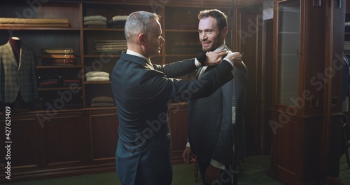 Cinematic shot of professional tailor taking measurements of client for creation custom tailored suit in a luxury tailoring atelier. Concept of fashion, handmade, hand craft, couturier and business.