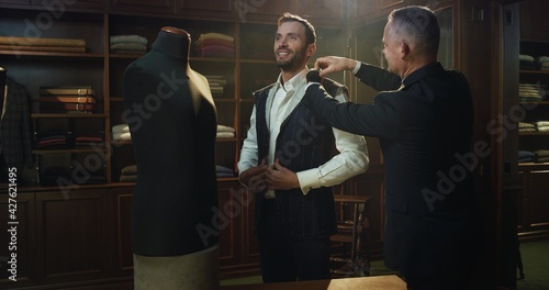 Cinematic shot of professional tailor taking measurements of client for creation custom tailored suit in a luxury tailoring atelier. Concept of fashion, handmade, hand craft, couturier and business.	 photo