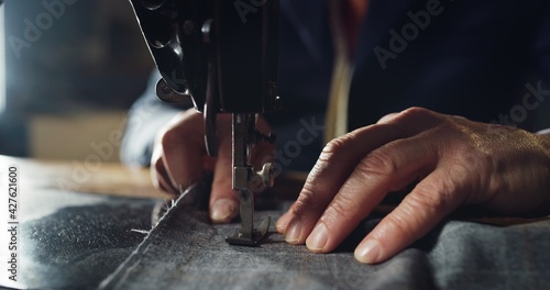 Macro shot of experienced tailor is sewing custom handmade high quality apparel in ancient luxury traditional tailoring workshop. Concept of industry, handmade, hand craft, couturier and tradition. photo