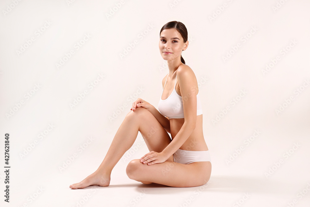 Studio shot of fit woman wearing seamless underwear in seating on the floor isolated on white. Slim attractive female with flat belly in white lingerie. Copy space, close up, background. Studio shot of fit woman wearing seamless underwear in seating on the floor isolated on white. Slim attractive female with flat belly in white lingerie. Copy space, close up, background.