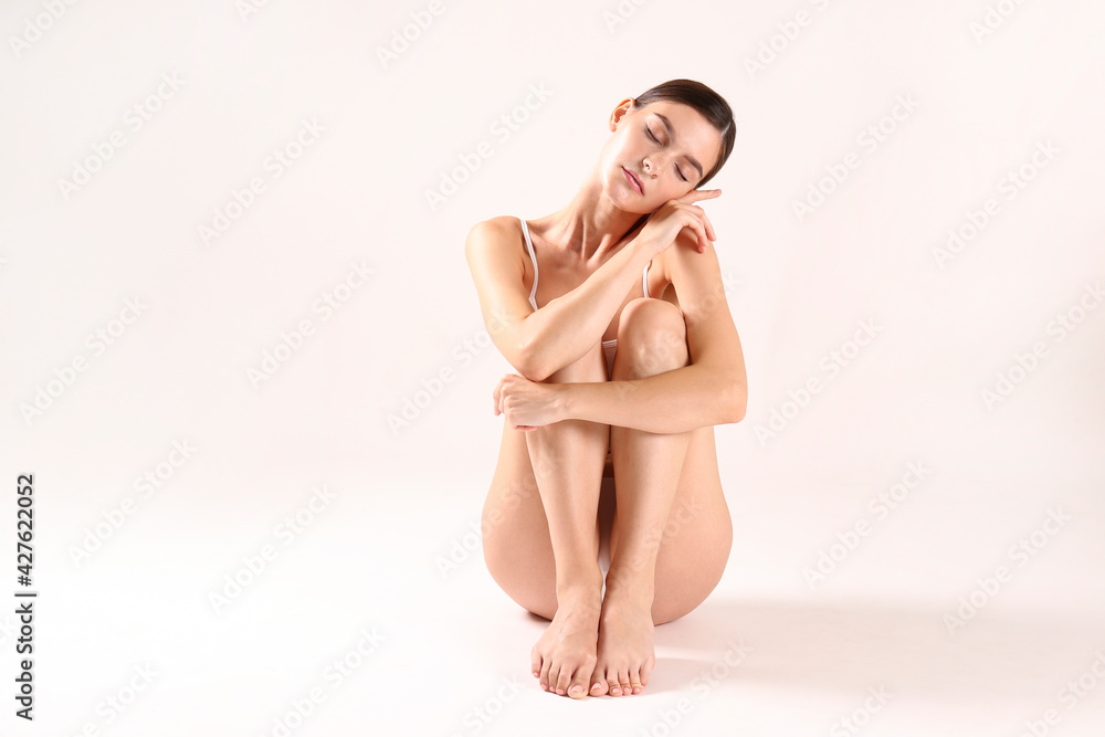 Obraz premium Studio shot of fit woman wearing seamless underwear in seating on the floor isolated on white. Slim attractive female with flat belly in white lingerie. Copy space, close up, background.