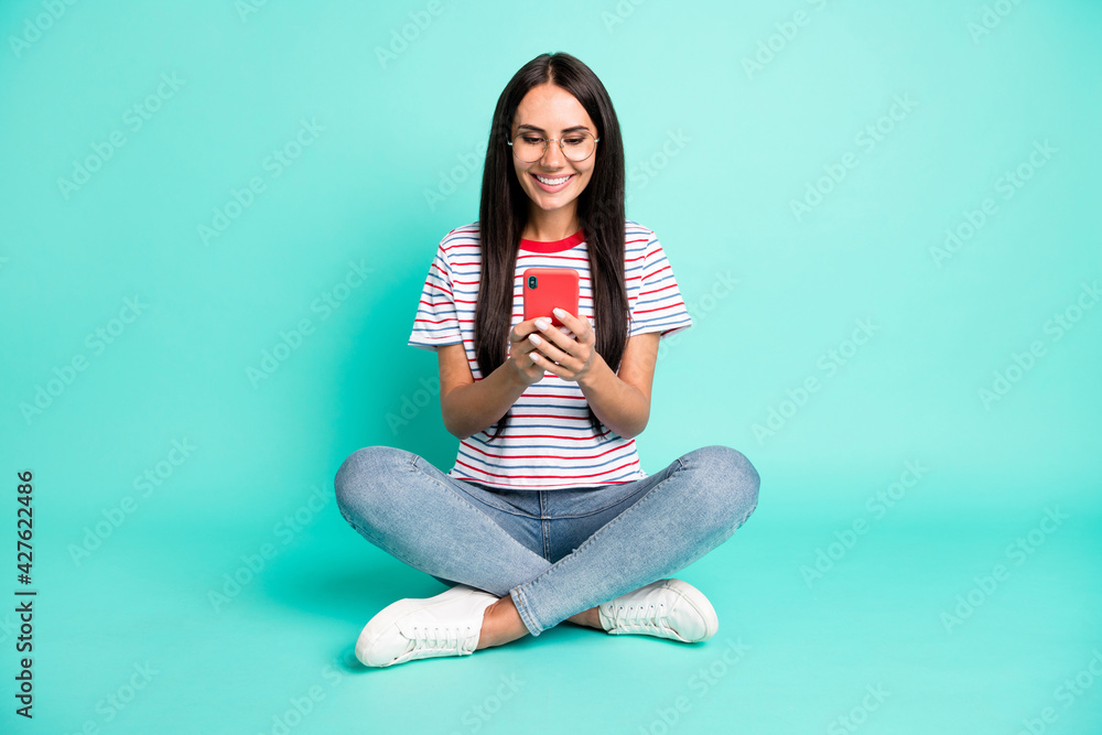 Full body portrait of charming positive lady sit look phone typing toothy smile isolated on turquoise color background