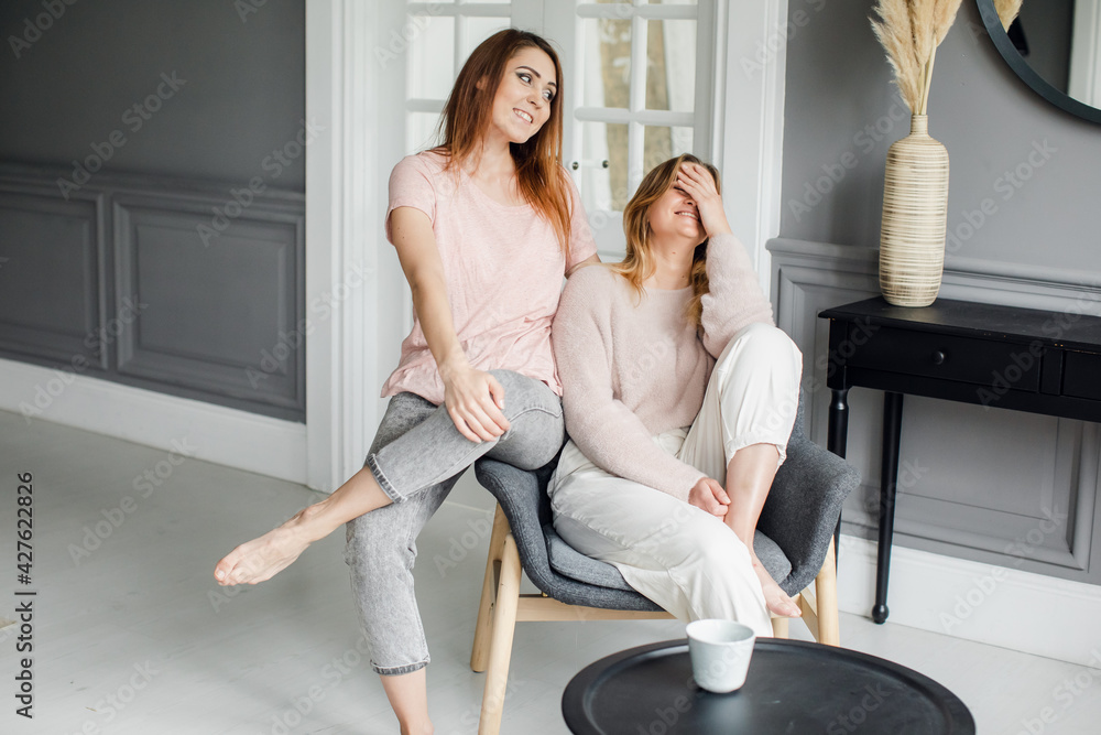 Two attractive girlfriends sitting on the sofa, talking excitedly, smiling Two attractive girlfriends sitting on the sofa, talking excitedly, smiling
