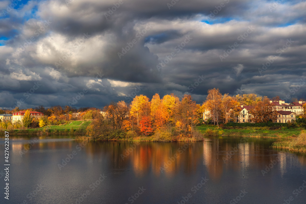 The sky before the storm. Bright autumn dramatic view of the village on the shore of the lake before a thunderstorm