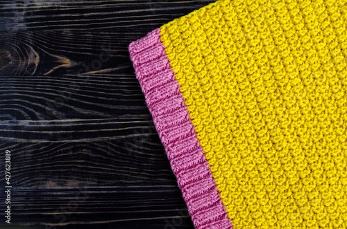 fabric knitted from yellow and pink threads on a dark wooden background top view of kopi space