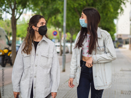 Mujeres jóvenes amigas paseando por la calle con mascarilla para protegerse del coronavirus 