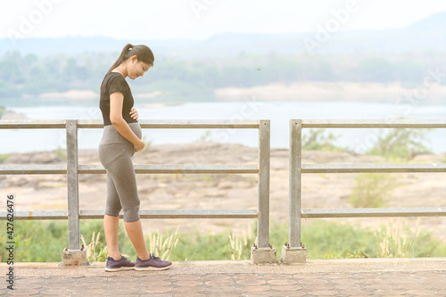 Portrait of young Asian pregnant woman walking and workout in the park. © nuttapon