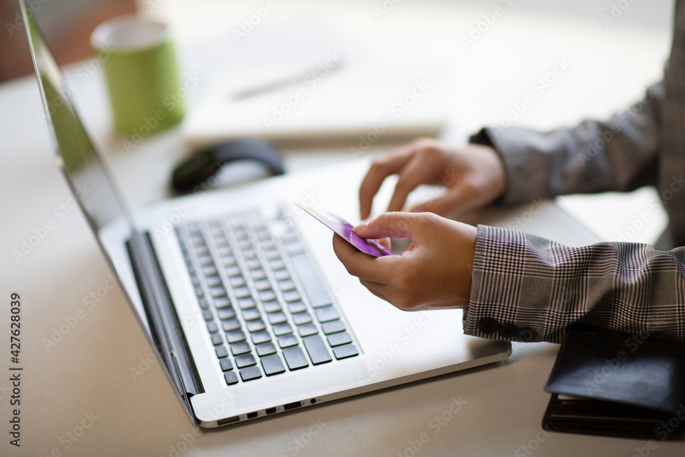 Fototapeta premium Young businesswoman holding a credit card and typing. On-line shopping on the internet using a laptop