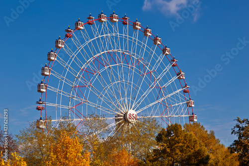 A ferris wheel against a background of blue sky and autumn trees with bright foliage