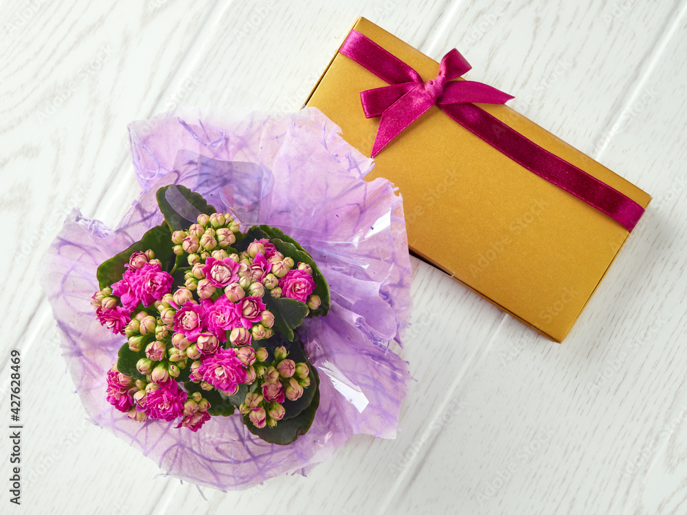 Top view to the bouquet of kalanchoe blossfeldiana with golden gift box and pink ribbon on the light gray floor. Top view to the bouquet of kalanchoe blossfeldiana with golden gift box and pink ribbon on the light gray floor.