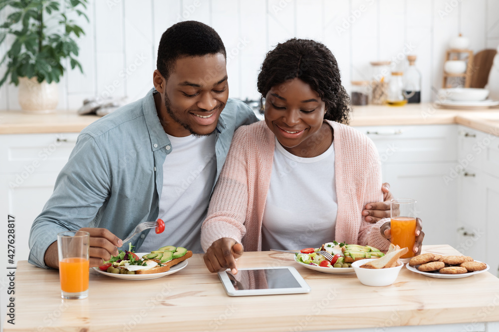 Young Black Millennial Spouses Shopping Online On Digital Tablet While Having Breakfast Young Black Millennial Spouses Shopping Online On Digital Tablet While Having Breakfast