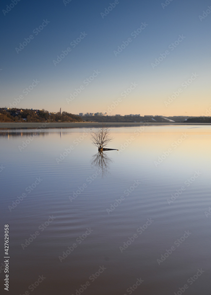 Cityscape at golden sunset with buildings reflecting in the lake. Silhouettes of ducks behind a bush sticking out of the water . Early spring season and remainings of semi-melted ice. Cityscape at golden sunset with buildings reflecting in the lake. Silhouettes of ducks behind a bush sticking out of the water . Early spring season and remainings of semi-melted ice.