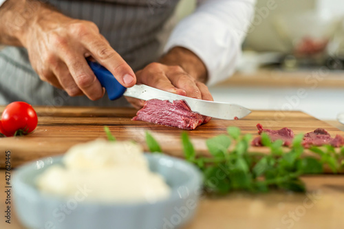 A close-up of the chef's hands cutting carpaccio