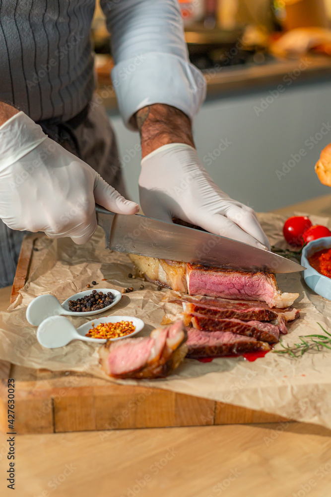 A close-up view of a cook cutting a grilled steak into thinner pieces on a wooden kitchen board