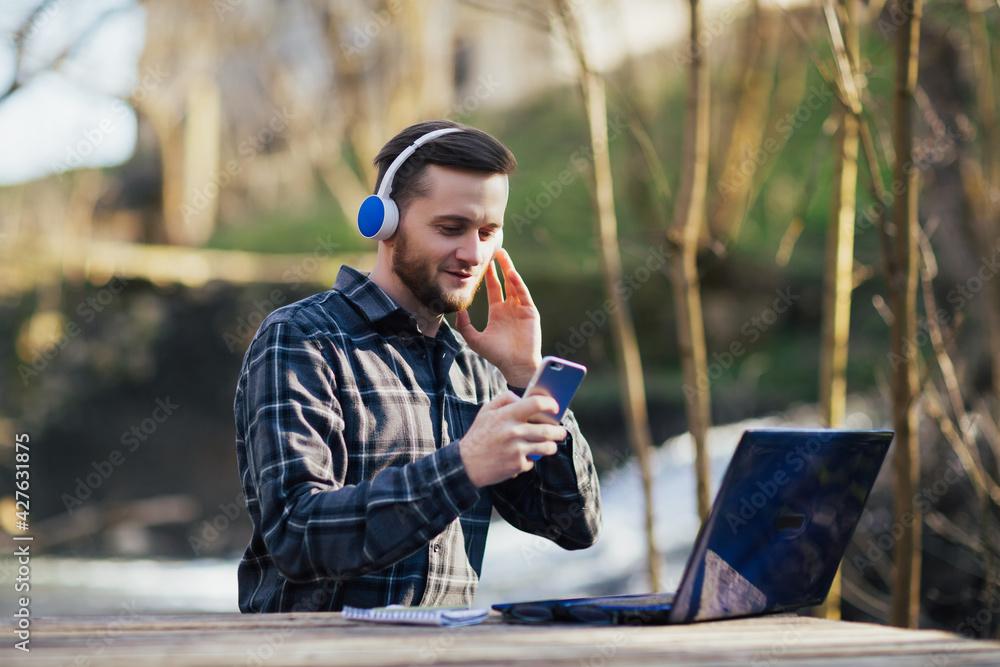 Man with headphones working on laptop and is using the smartphone at natural rough wooden desk. Man with headphones working on laptop and is using the smartphone at natural rough wooden desk.