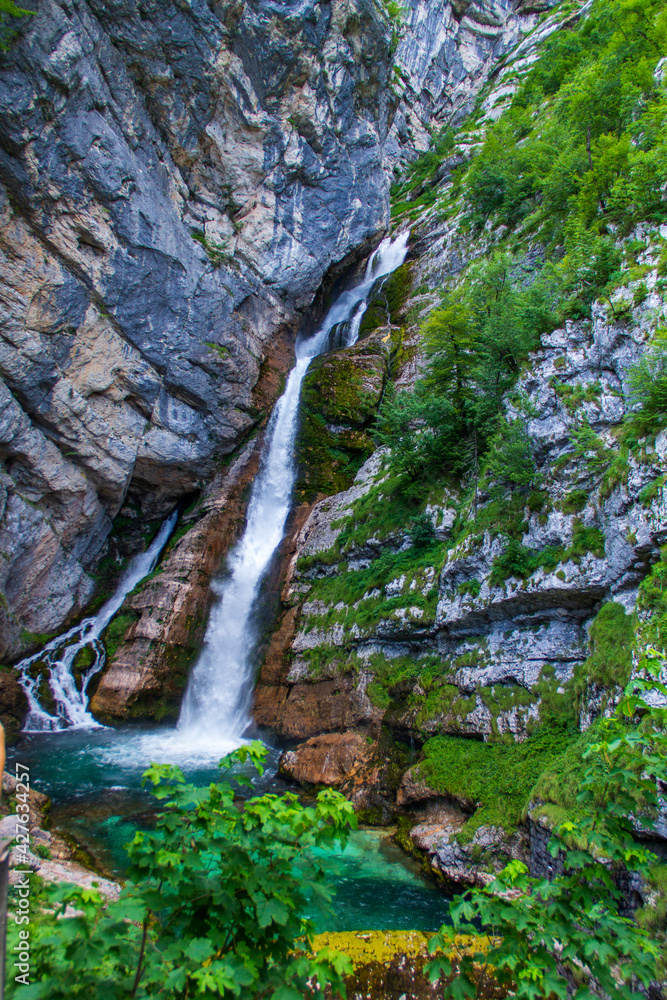 Waterfall in Slovenian mountains falling from rock to small lake.