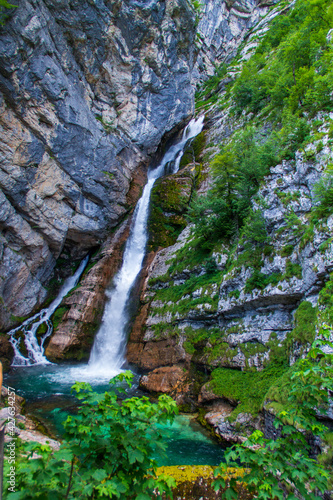 Waterfall in Slovenian mountains falling from rock to small lake.