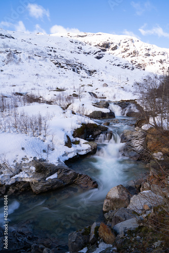 Røldal waterfall at the end of winter, mountain slopes covered with snow photo