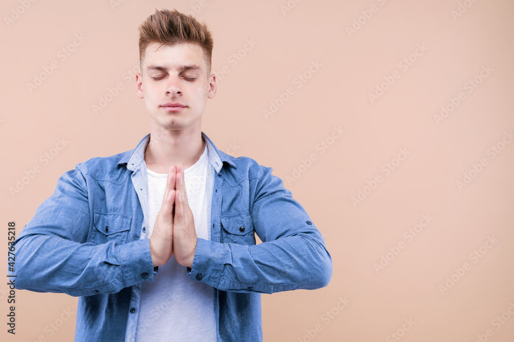 His soul is calm and relieved. Portrait of focused and determined peaceful young male student gathering courage and patience as meditating holding hands in pray or namaste gesture with closed eyes His soul is calm and relieved. Portrait of focused and determined peaceful young male student gathering courage and patience as meditating holding hands in pray or namaste gesture with closed eyes
