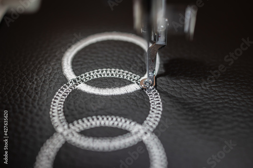 Machine embroidery of circles with white thread on black leather fabric.